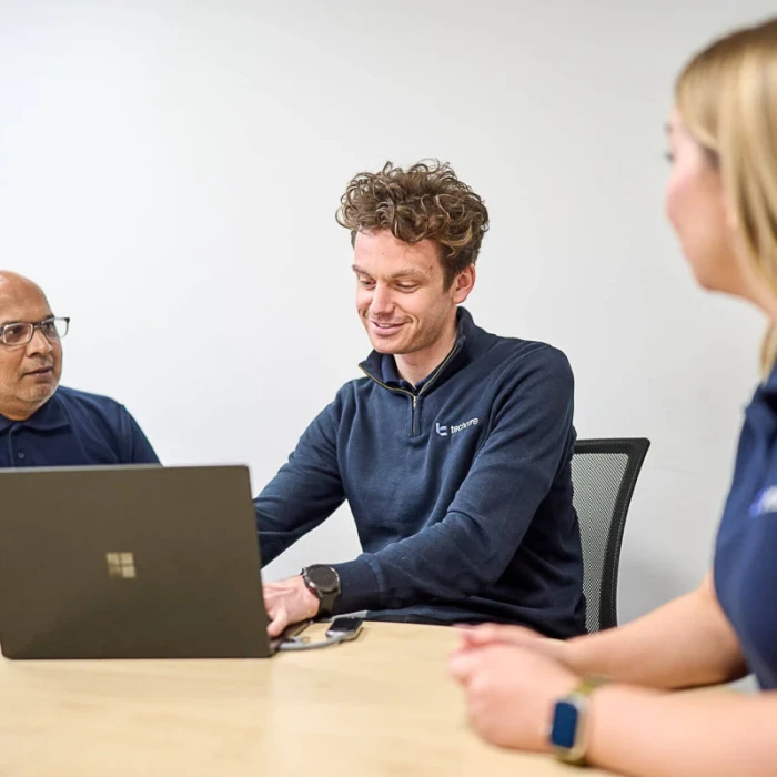 Two men and one woman sat around a laptop wearing Techcare uniform