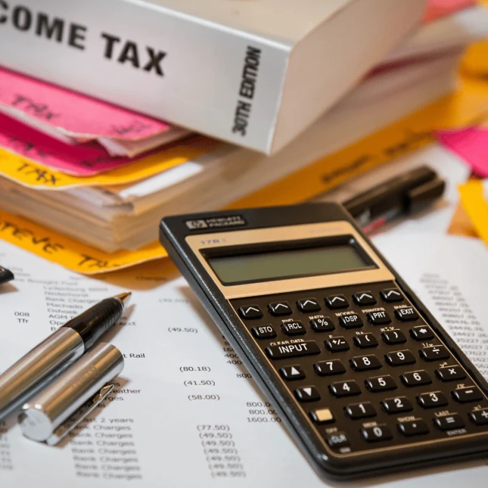 A calculator, pen, and sheets of paper showing financial figures