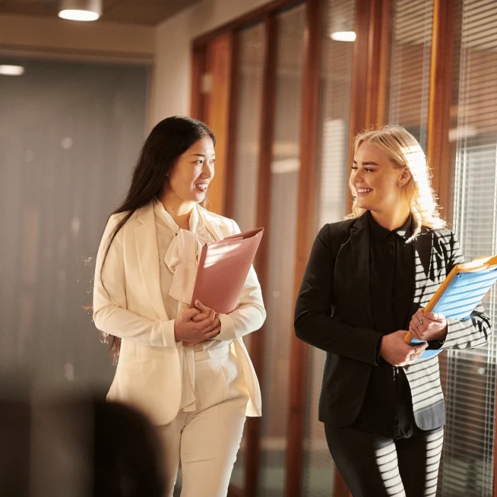 Two female lawyers in suits walking down a corridor holding paperwork