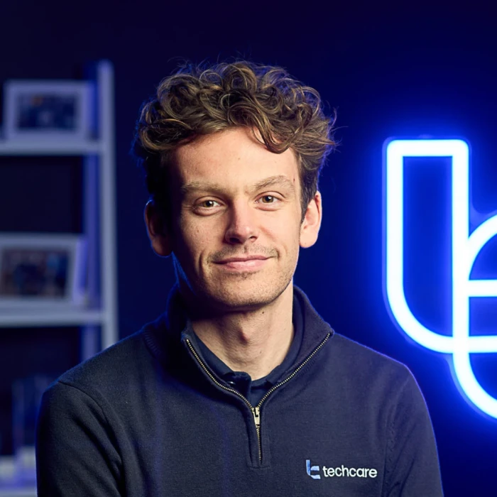 A young man with short, curly brown hair. He's wearing a navy jumper.