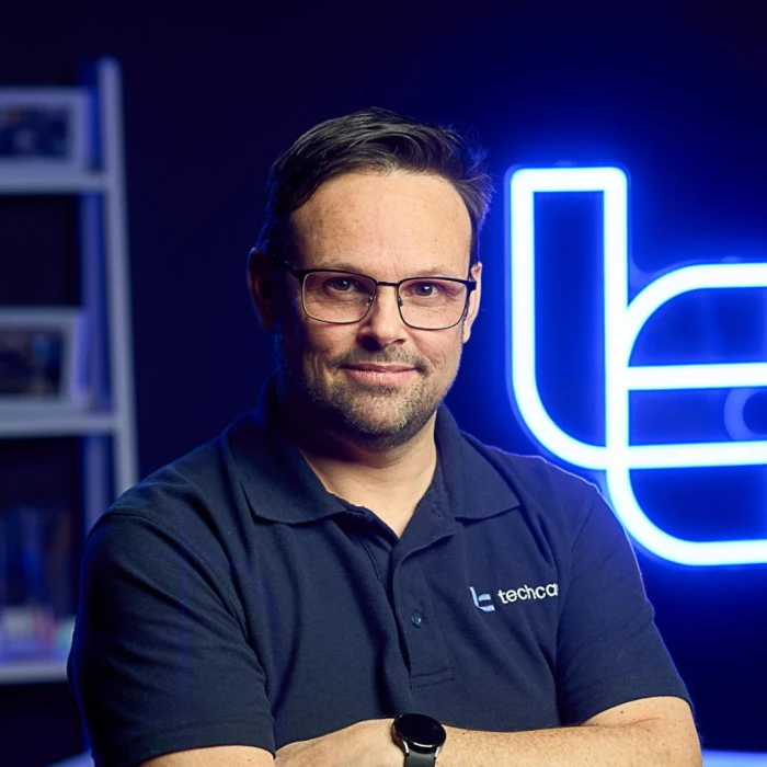 A man with short brown hair and glasses wearing a navy shirt.