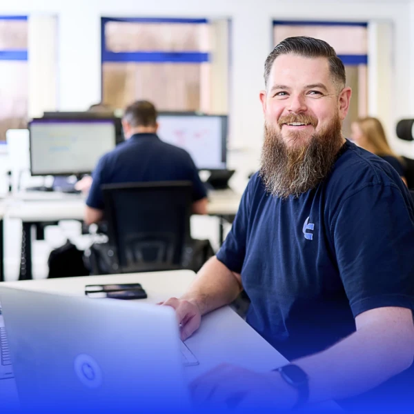 A man with short hair and a beard working on a desk in a brightly lit office