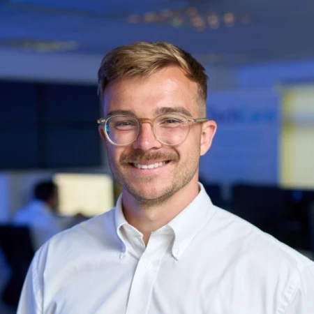 A man with light hair, glasses and a moustache wearing a white shirt. 